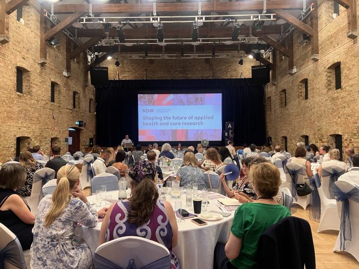 Attendees seated at round tables during the NIHR ARC East of England launch event, listening to a presentation 