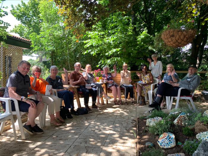 Members of the dementia involvement group sitting outside and waving at the camera